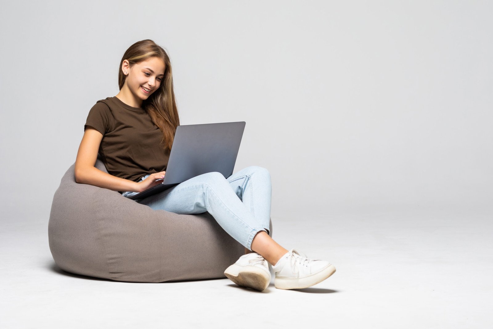 Happy woman sitting on the floor using laptop on gray background